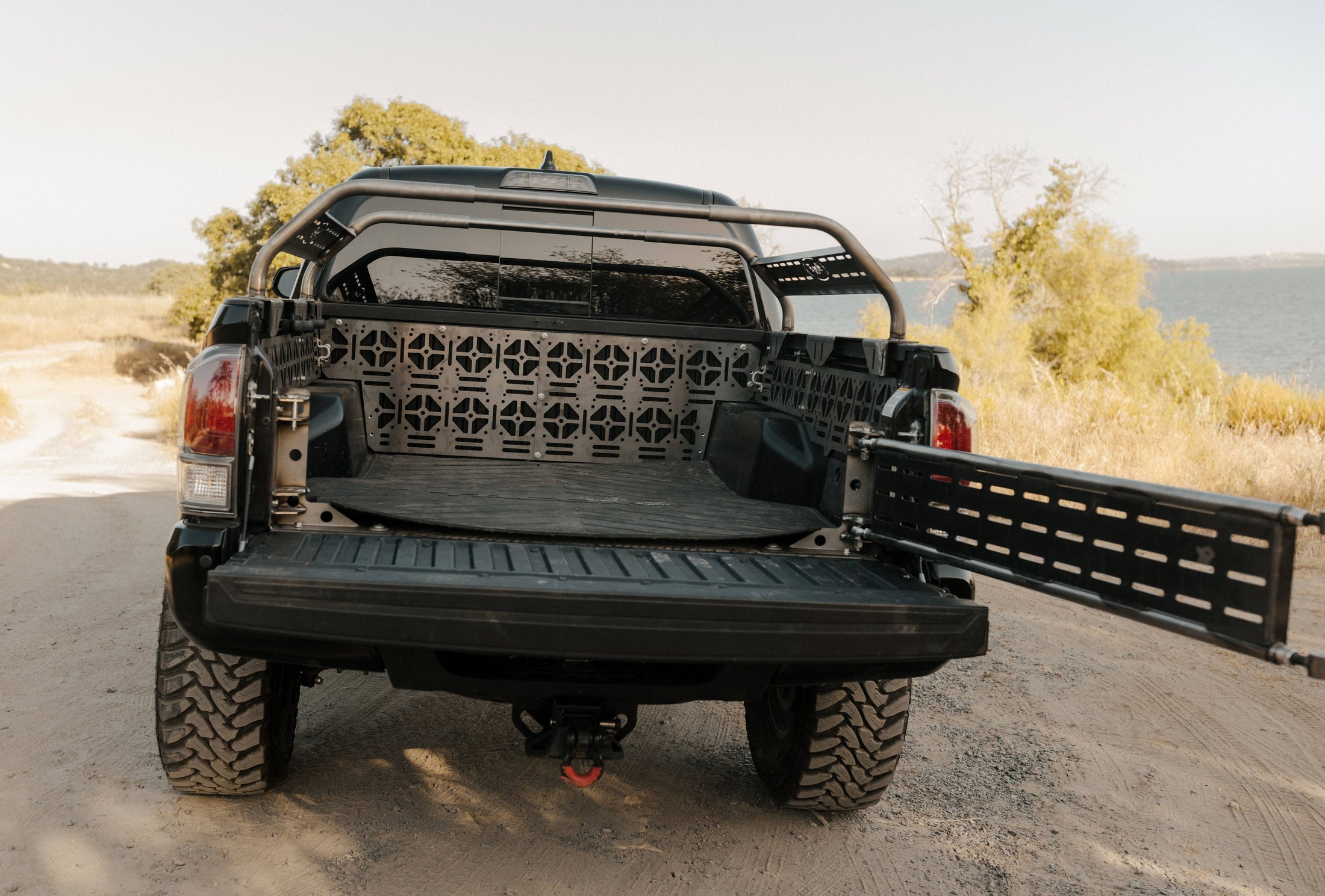 a black truck parked on a dirt road next to a body of water