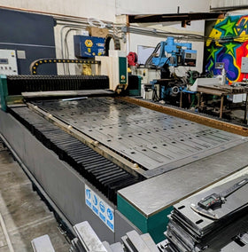Large industrial laser cutting machine in a workshop with various tools and equipment.